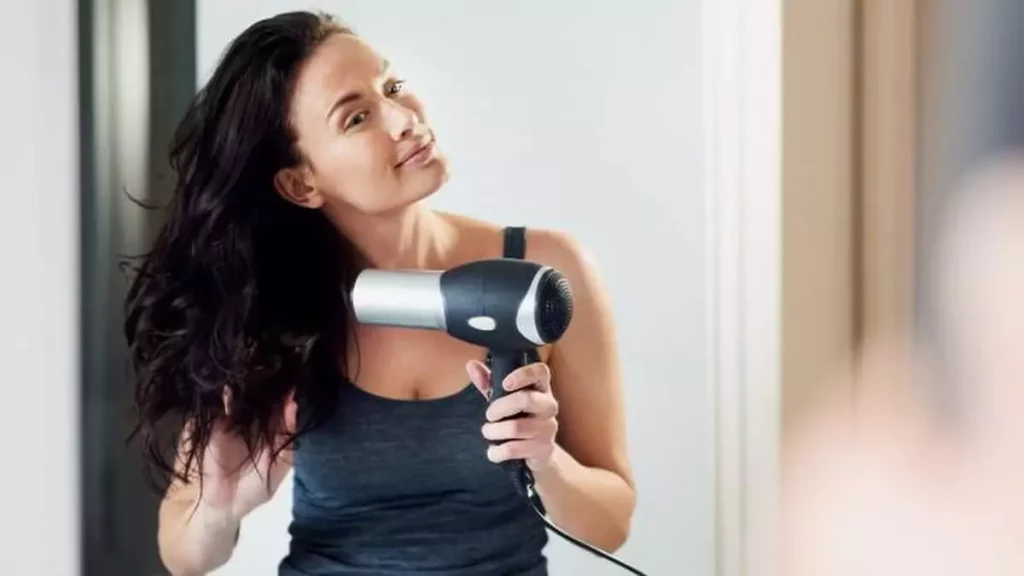 Imagem destaque do post sobre como usar secador de cabelo: Mulher secando os cabelos em frente ao espelho